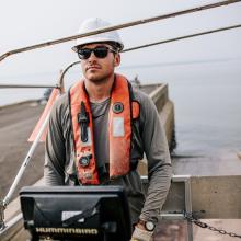 Englobe employee standing on boat in front on a hydrology tool