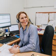 female employee working at her desk at Englobe office, she is wearing a headset and smiling