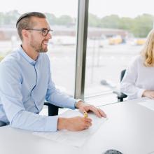 two employees sitting in a board room with large windows behind them
