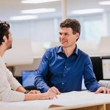 Two male employees standing at a desk and reviewing documents together