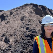 Ginette Coulombe wearing PPE and standing in front of a pile of compost