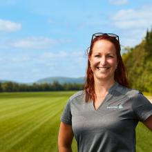 A woman wearing an Englobe tshirt standing in front of a field and a blue sky