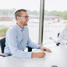 two employees sitting in a board room with large windows behind them