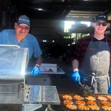 Ed Collins and Richard Twiss preparing burgers behind a BBQ