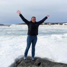 Photo of Lydia Charbonneau happy, arms and hands in the air, by the icy waterfront in Nunavik