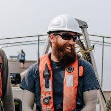 photo of 3 smiling engineers working on an environnemental study on boat with white helmet and sunglasses