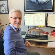 portrait of Luc Chartrand sitting at his desk smiling at camera