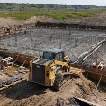 Construction site showing excavation and concrete foundation work with steel rebar, formwork, and heavy equipment used for infrastructure development.