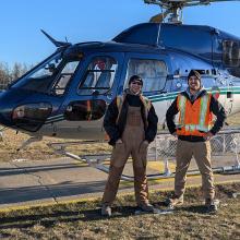 picture of two englobe's employees standing in front of an helicopter