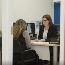Two coworkers working together at a table in an industrial workspace, reviewing material samples and tools.