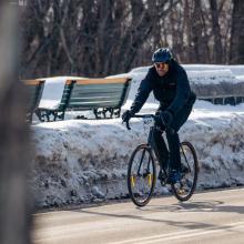 David Desrochers riding on a cleared winter road during the Snow Pentathlon, wearing cold‑weather gear and passing snowy benches and trees.