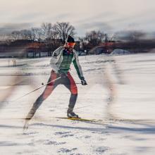 Martin Fleury — cross‑country skier moving across a snowy course with motion blur emphasizing speed and distant trees in the background.