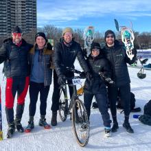 Englobe team members posing outdoors at the Pentathlon des neiges with skis, a bike, and snowshoes on a snowy course.