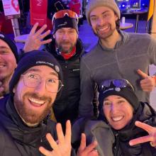 Englobe Snow Pentathlon team taking a lively selfie together, surrounded by colorful lights and event tents.