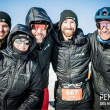 Englobe team members wearing matching winter jackets posing outdoors during the Pentathlon des neiges, with buildings and event structures visible in the background.