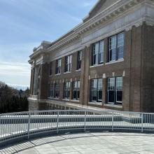 Exterior view of the Victoria High school building featuring a modern glass addition and a gently sloped metal accessibility ramp, under a clear blue sky.