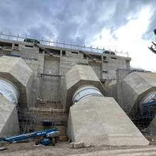 Concrete dam interior under construction with extensive scaffolding, steel platforms, and access stairs surrounding structural and mechanical components.